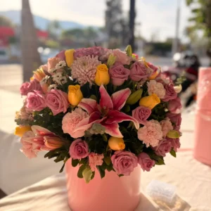Arreglo floral redondo en base rosa con rosas y flores mixtas en tonos rosa coral y amarillo