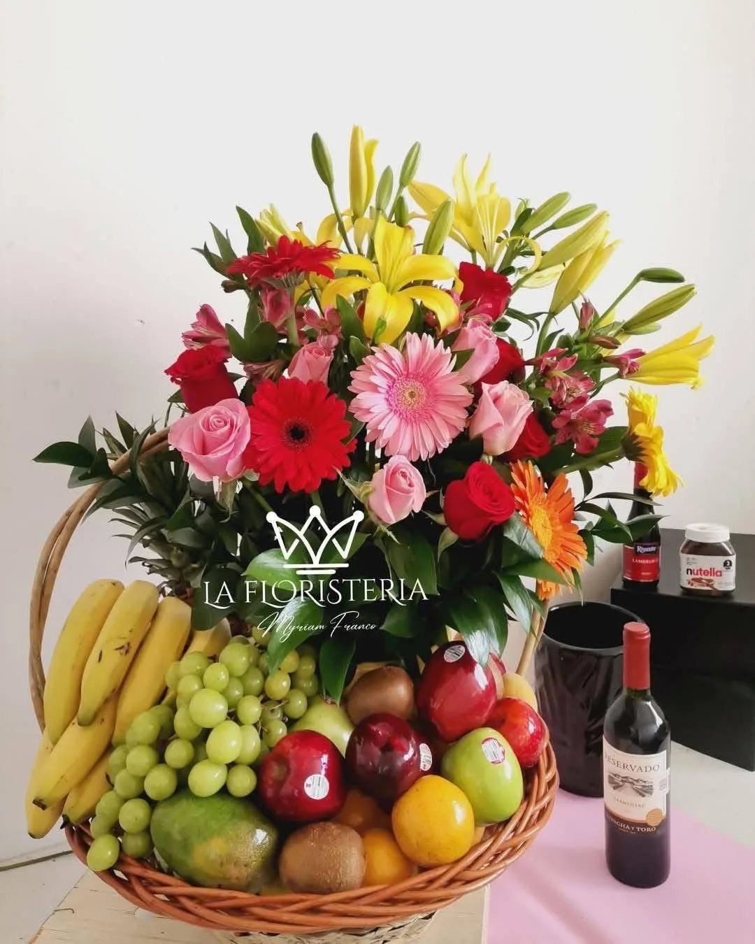 Canasta frutal con flores mixtas en tonos rojos rosas y amarillos