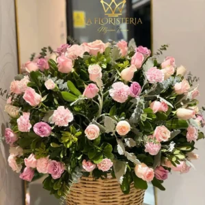 Canasta floral con rosas y claveles en tonos rosados y follaje verde