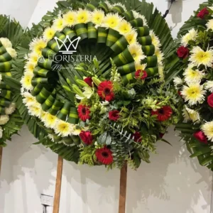 Corona fúnebre blanca con flores rojas y follaje verde en base circular